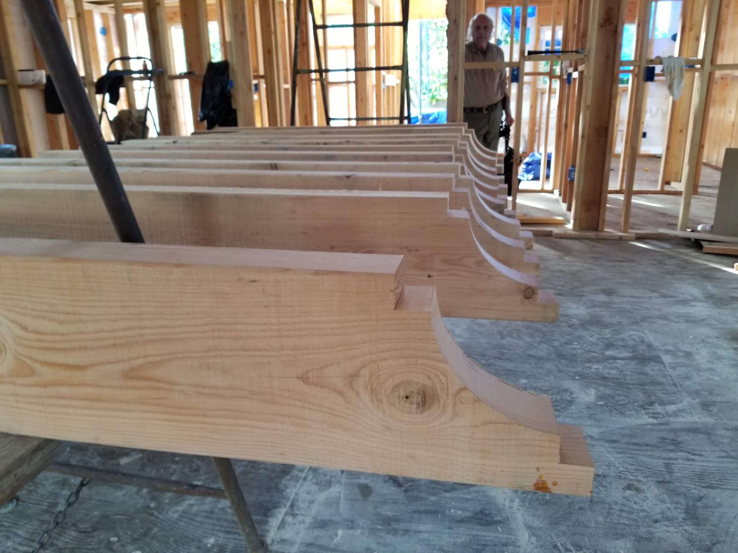 Wooden beams with decorative carvings, organized in a construction site with wooden framing in the background.