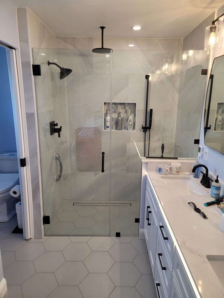 Double sink bathroom with glass shower and white hexagon floor tiles.