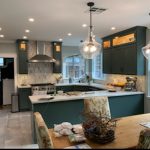 Modern kitchen with dark green cabinets, a large island, stainless steel appliances, and pendant lighting, featuring a cozy dining area.
