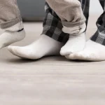 How long before you can walk on newly installed flooring. Person standing in socks on newly installed hardwood flooring, waiting before walking fully to protect the surface.